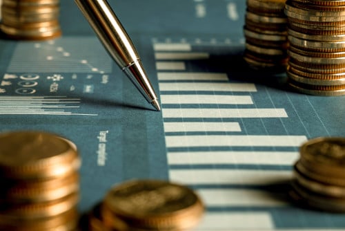 Pen pointing at data chart surrounded by coins